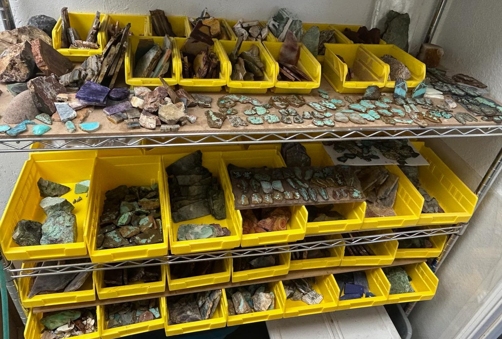 Racks of bins in the shop filled with rough and slabbed turquoise, chrysocolla and jasper, with more slab pieces on the shelf above.